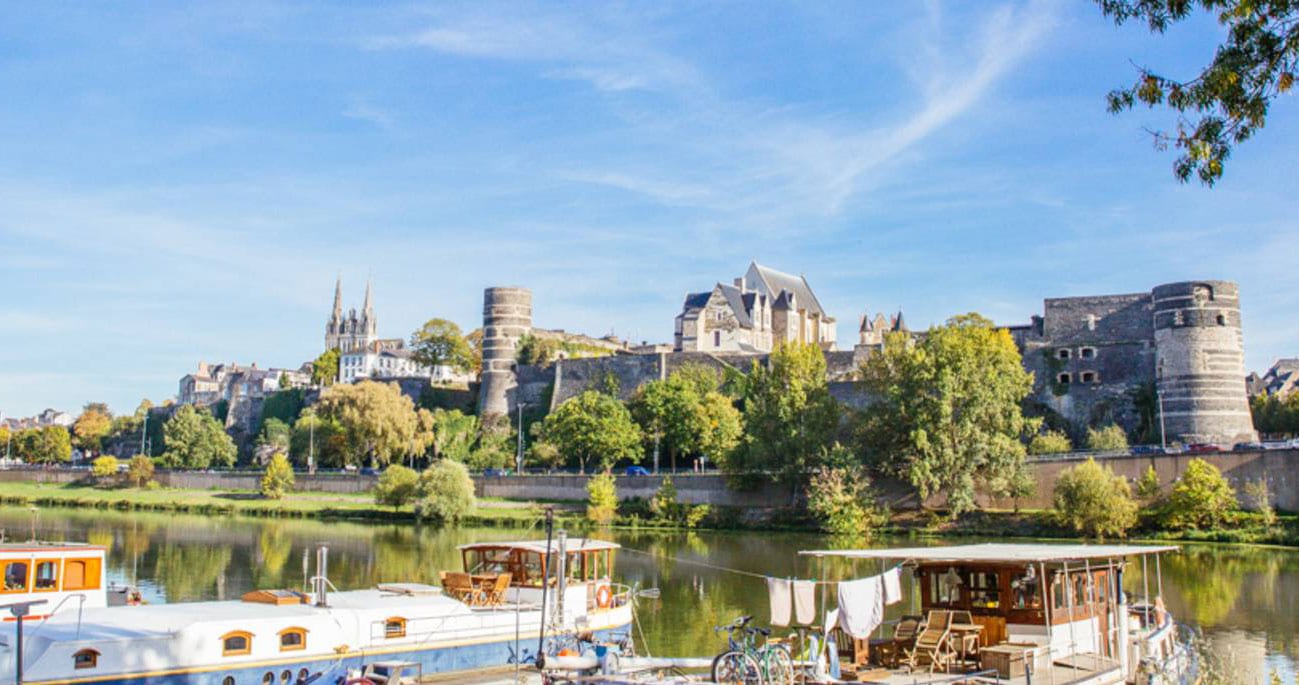 Vue du château d’Angers depuis la rivière avec des péniches au premier plan.
