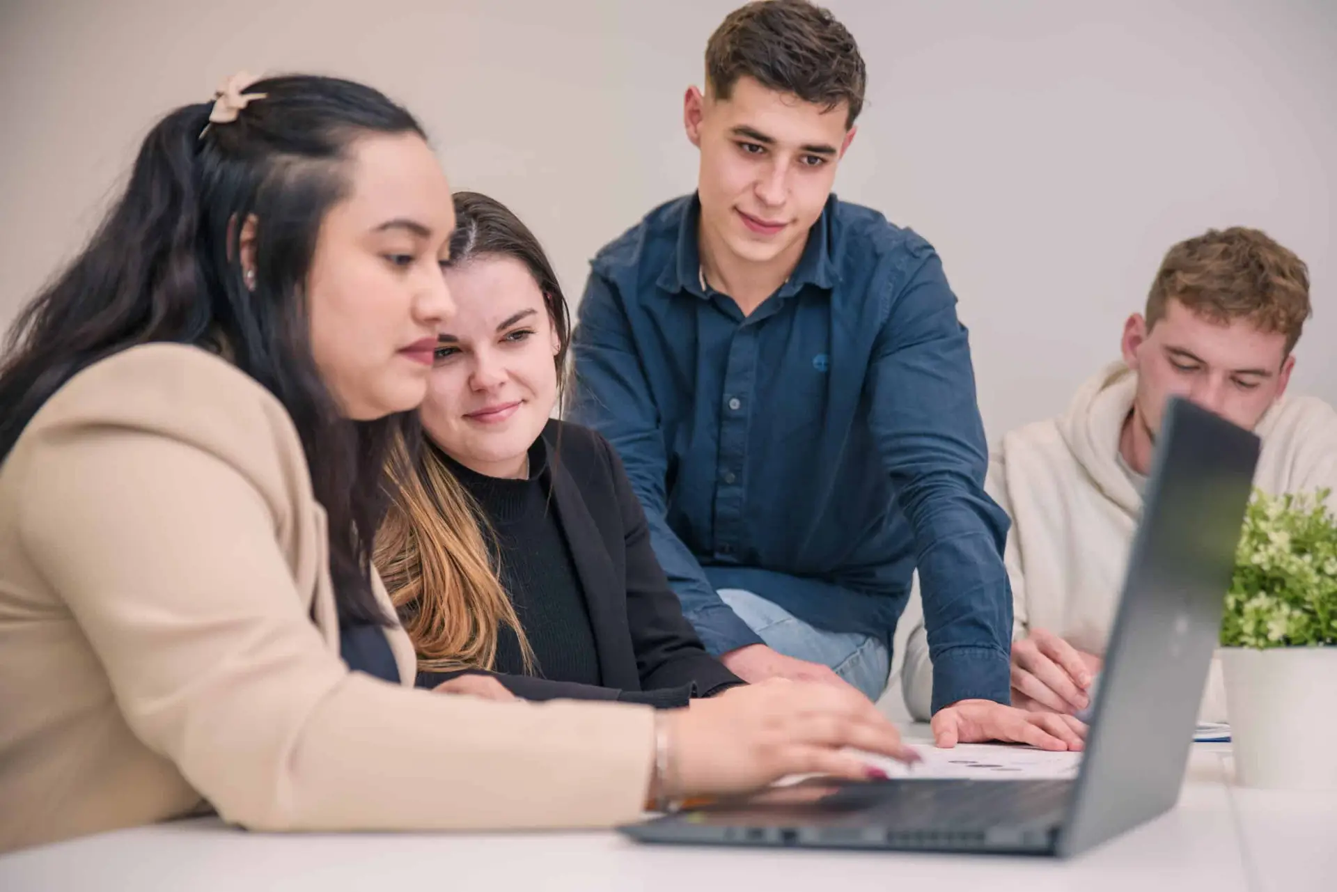Photo de quatre étudiants dont un assis sur la table, travaillant ensemble sur un ordinateur
