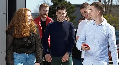 Groupe d'étudiants souriant devant le campus en allant en cours