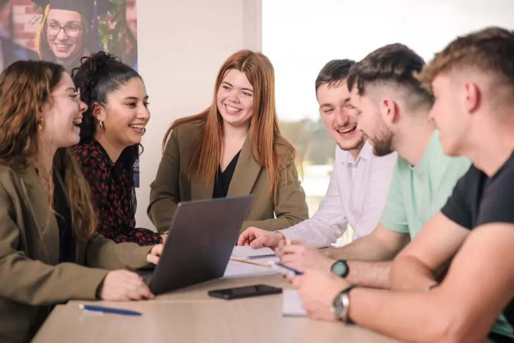 Photo de six étudiants rigolant et travaillant ensemble assis autour d'une table